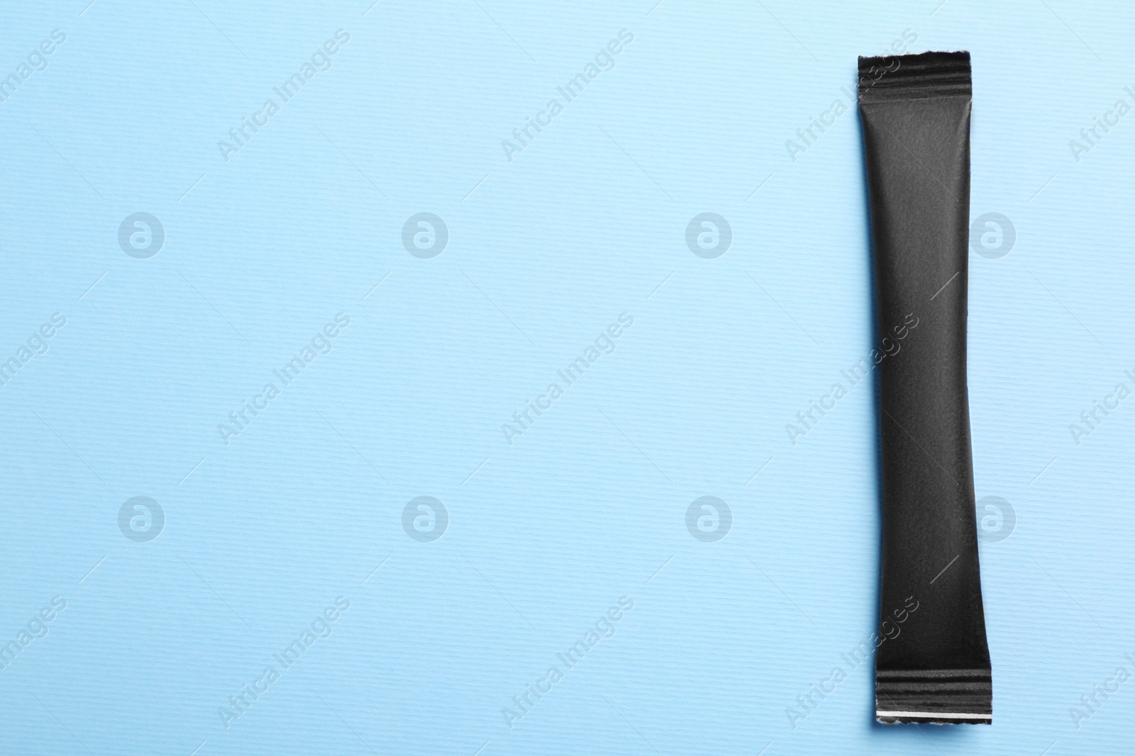 Photo of Black stick of sugar on light blue background, top view. Space for text