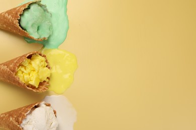 Photo of Melted ice cream in wafer cones on pale yellow background, flat lay. Space for text