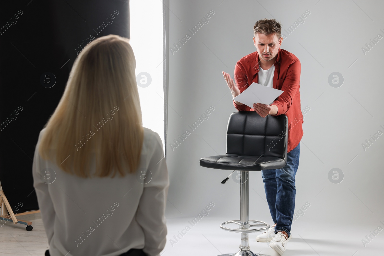 Photo of Man with script performing in front of casting director against light grey background in studio