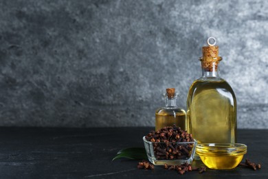 Photo of Essential oil and dried cloves on black table. Space for text