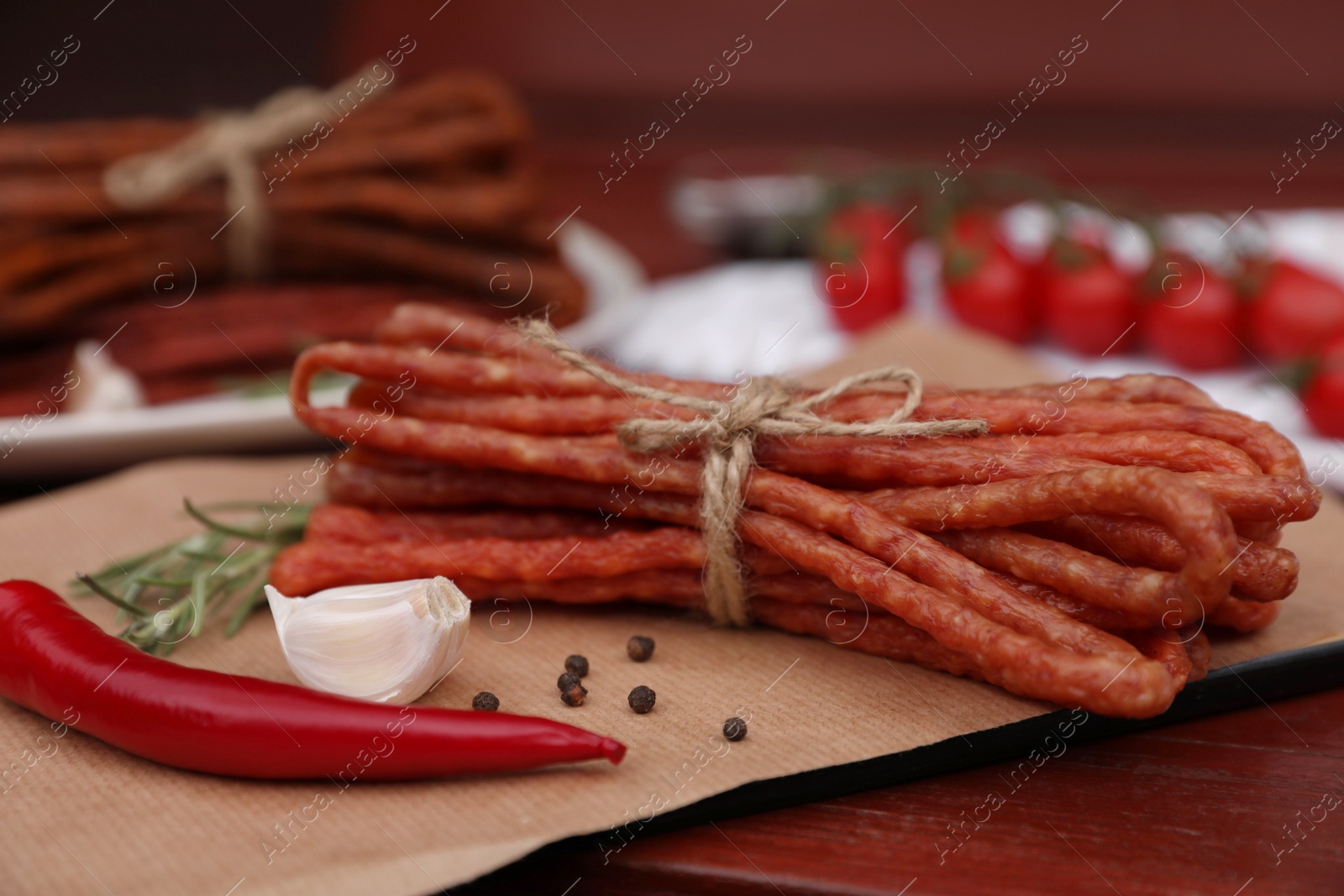 Photo of Bundles of delicious kabanosy with garlic, chilli and peppercorn on wooden table, closeup