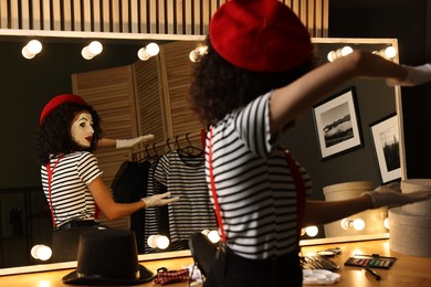 Young woman in mime costume posing near mirror indoors