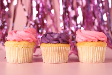 Photo of Delicious cupcakes with bright cream and confetti on pink background