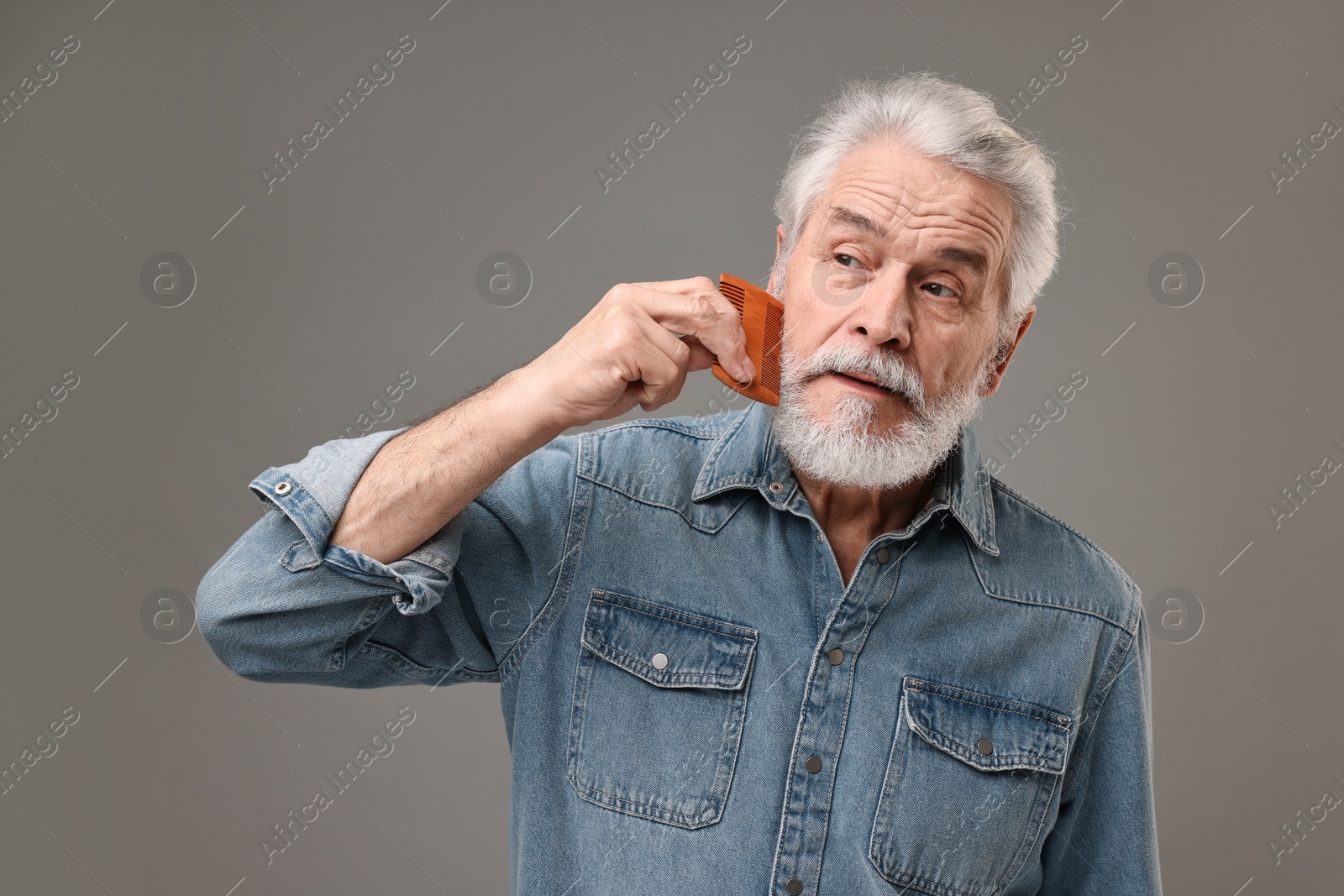 Photo of Senior man combing beard on grey background