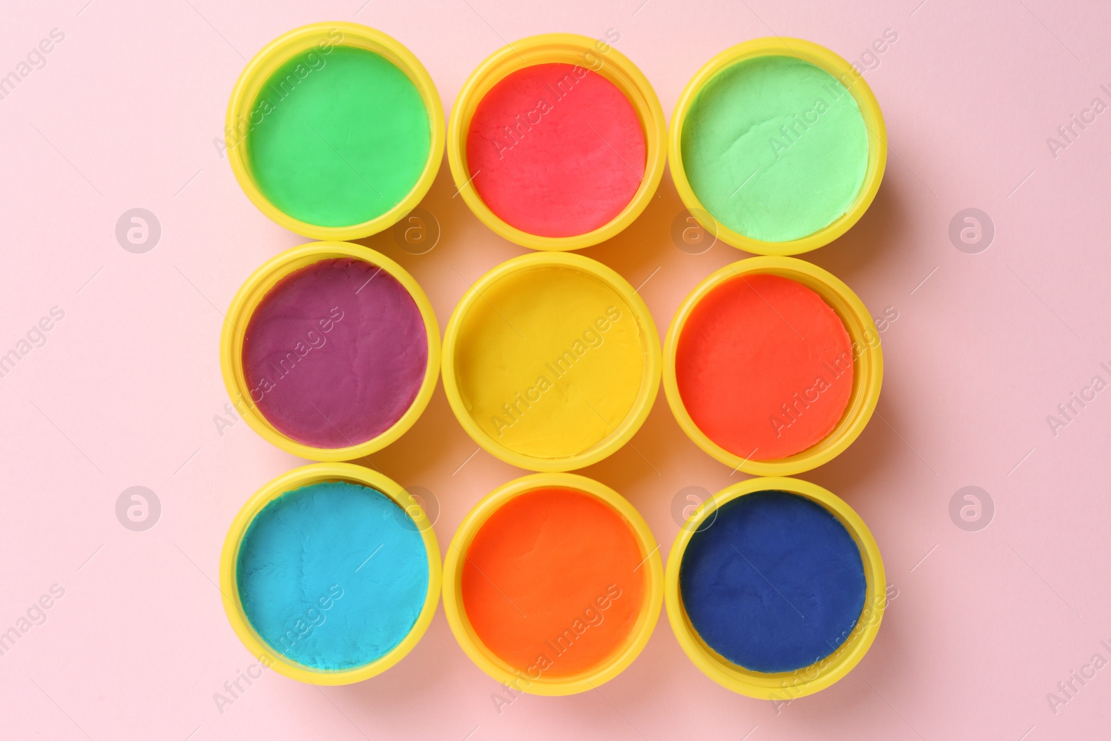 Photo of Plastic containers with colorful play dough on pink background, flat lay