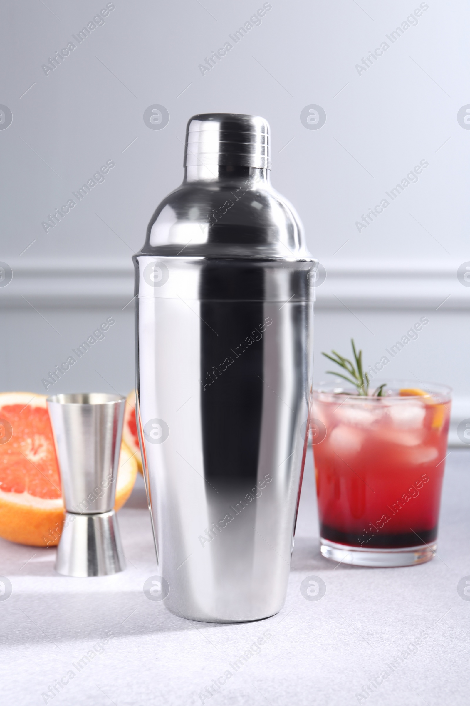 Photo of Metal shaker, delicious cocktail, jigger and grapefruit on light grey table