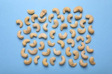 Many tasty cashew nuts on light blue background, top view