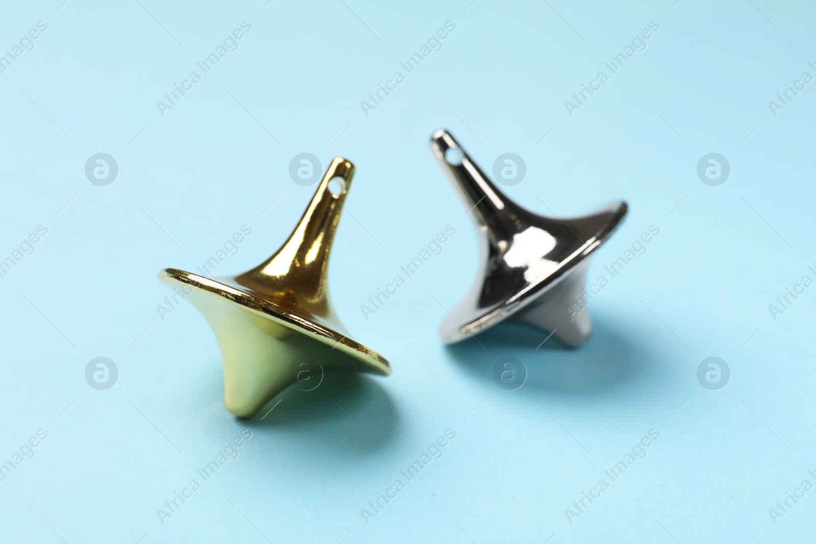 Photo of Golden and silver spinning tops on light blue background, closeup