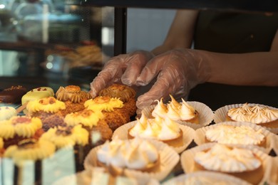 Photo of Seller taking delicious dessert from showcase in bakery shop, closeup