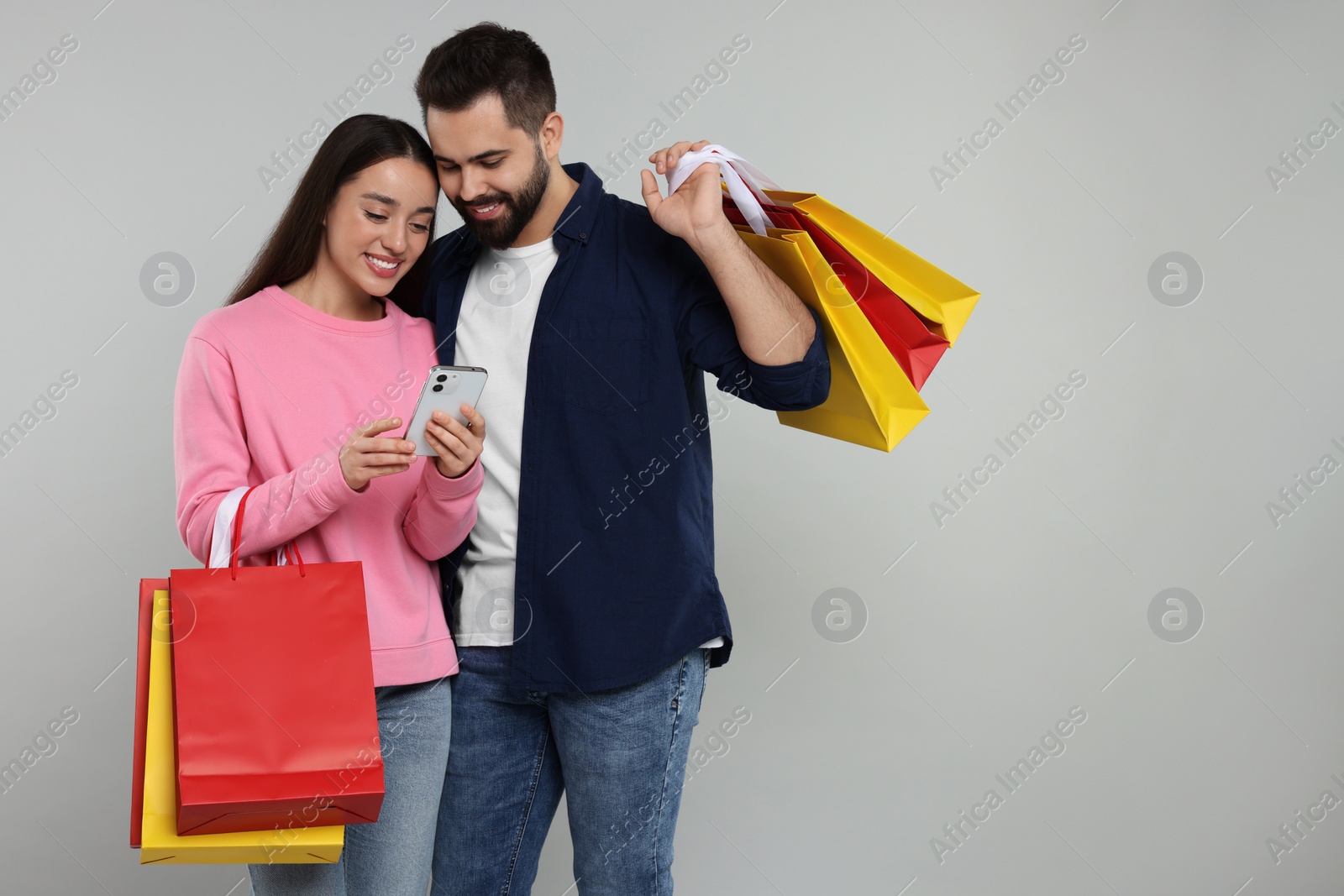 Photo of Happy couple with shopping bags and smartphone on grey background. Space for text