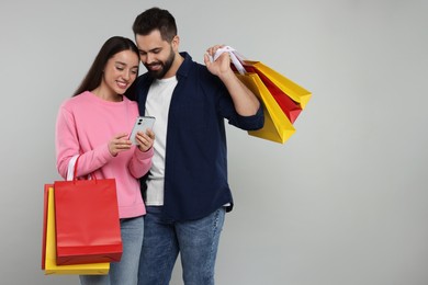 Happy couple with shopping bags and smartphone on grey background. Space for text