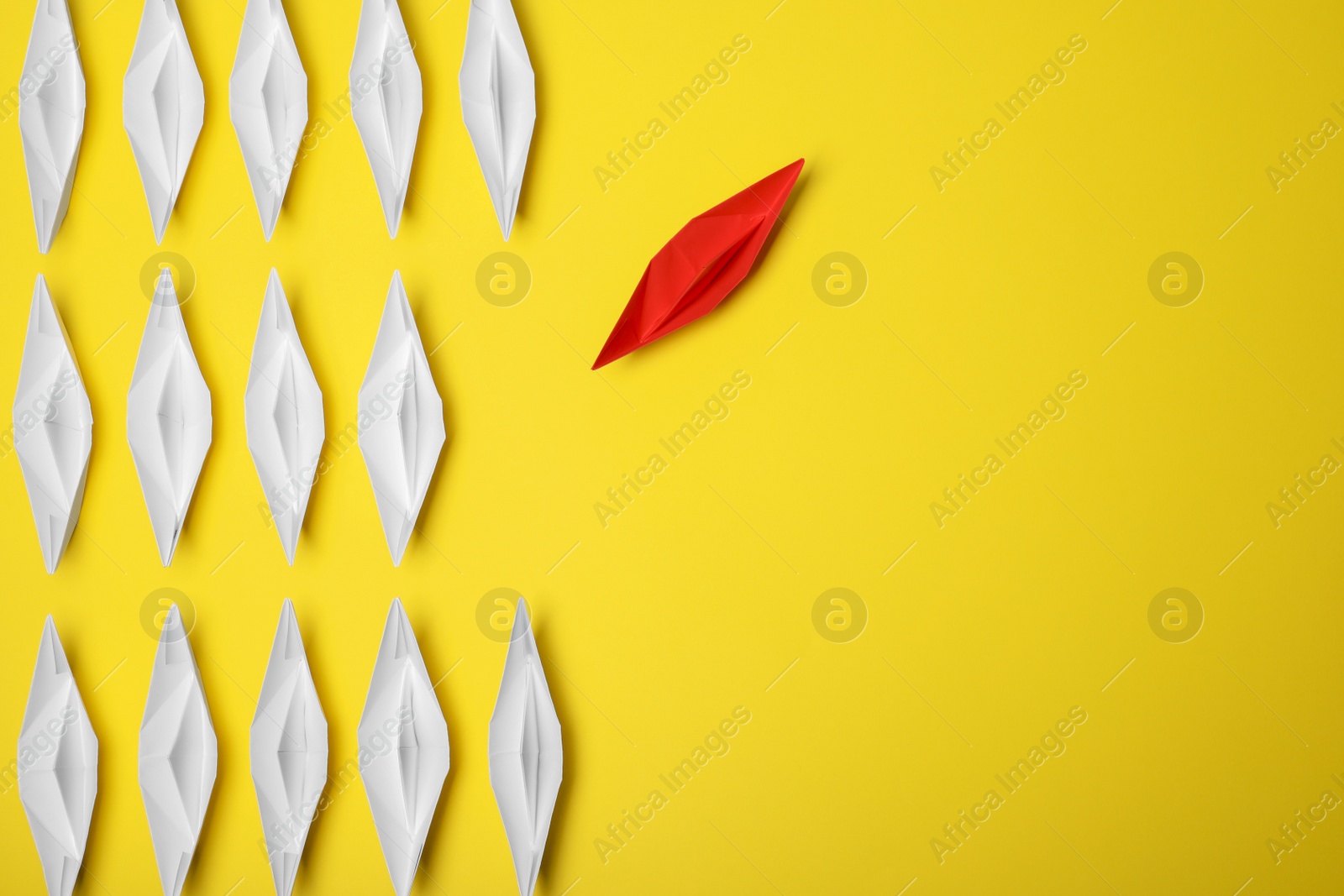 Photo of Red paper boat floating away from others on yellow background, flat lay with space for text. Uniqueness concept