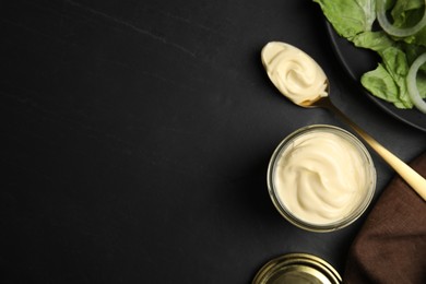 Photo of Jar and spoon with delicious mayonnaise near fresh salad on black table, flat lay. Space for text