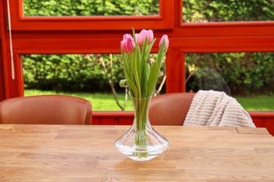 Photo of Pink tulips in glass vase on wooden table at terrace
