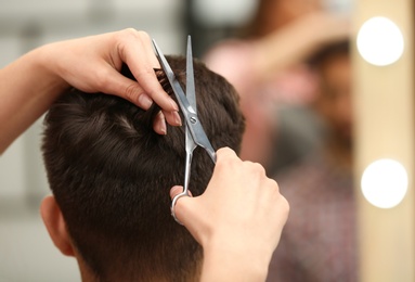 Barber making stylish haircut with professional scissors in beauty salon, closeup