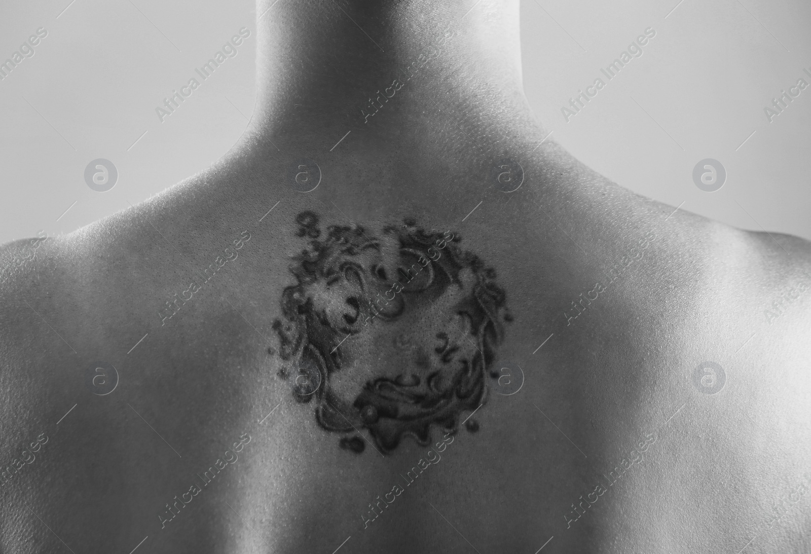 Image of Young woman with tattoo on light background, back view. Black and white photography