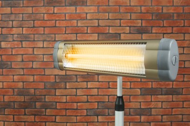 Electric infrared heater near red brick wall, closeup