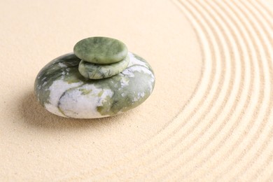 Photo of Zen garden stones on beige sand with pattern. Space for text