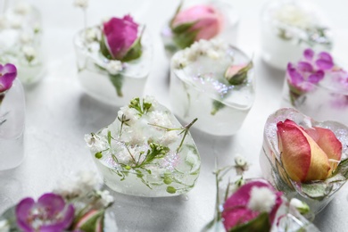 Photo of Heart shaped ice cubes with flowers on light background, closeup