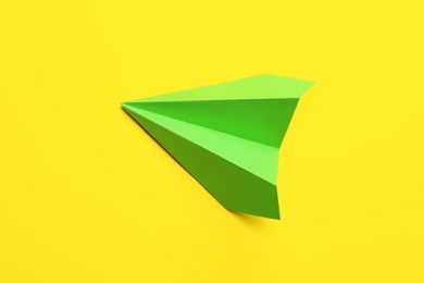 Photo of Green paper plane on yellow background, top view