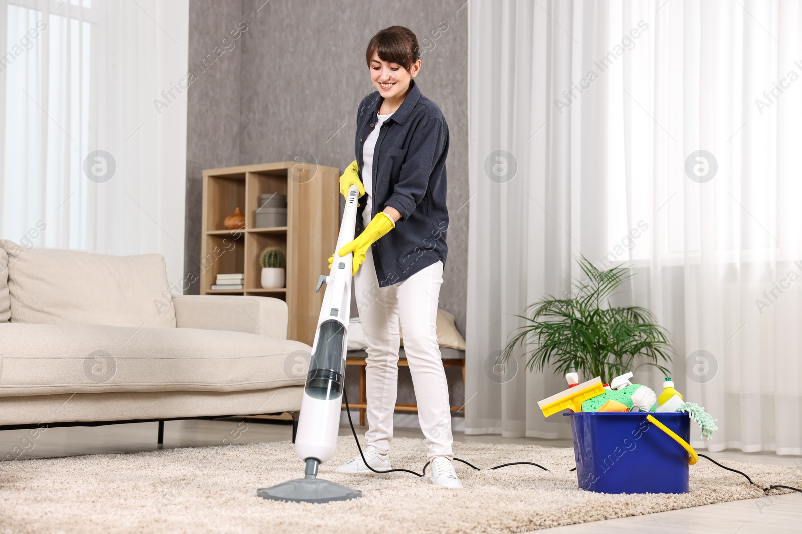 Photo of Happy young housewife vacuuming carpet at home