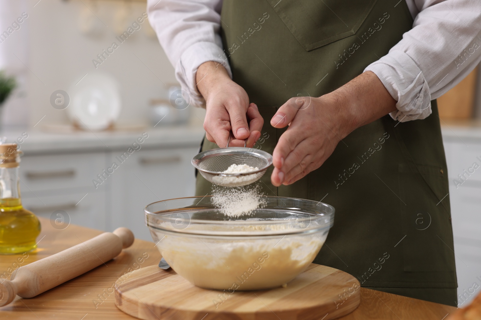 Photo of Making bread. Man sprinkling flour onto dough at wooden table in kitchen, closeup