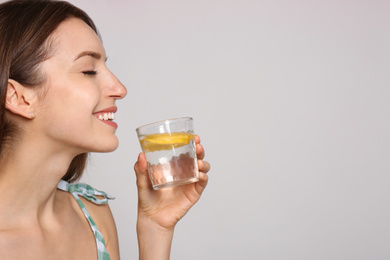 Young woman with glass of lemon water on light background. Space for text