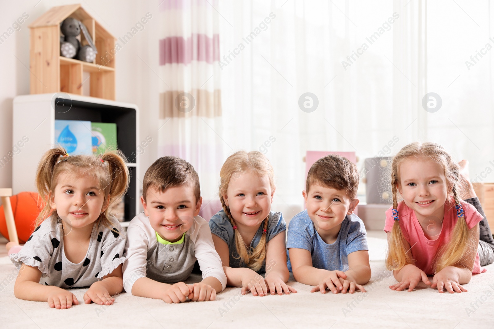 Photo of Playful little children lying on carpet indoors