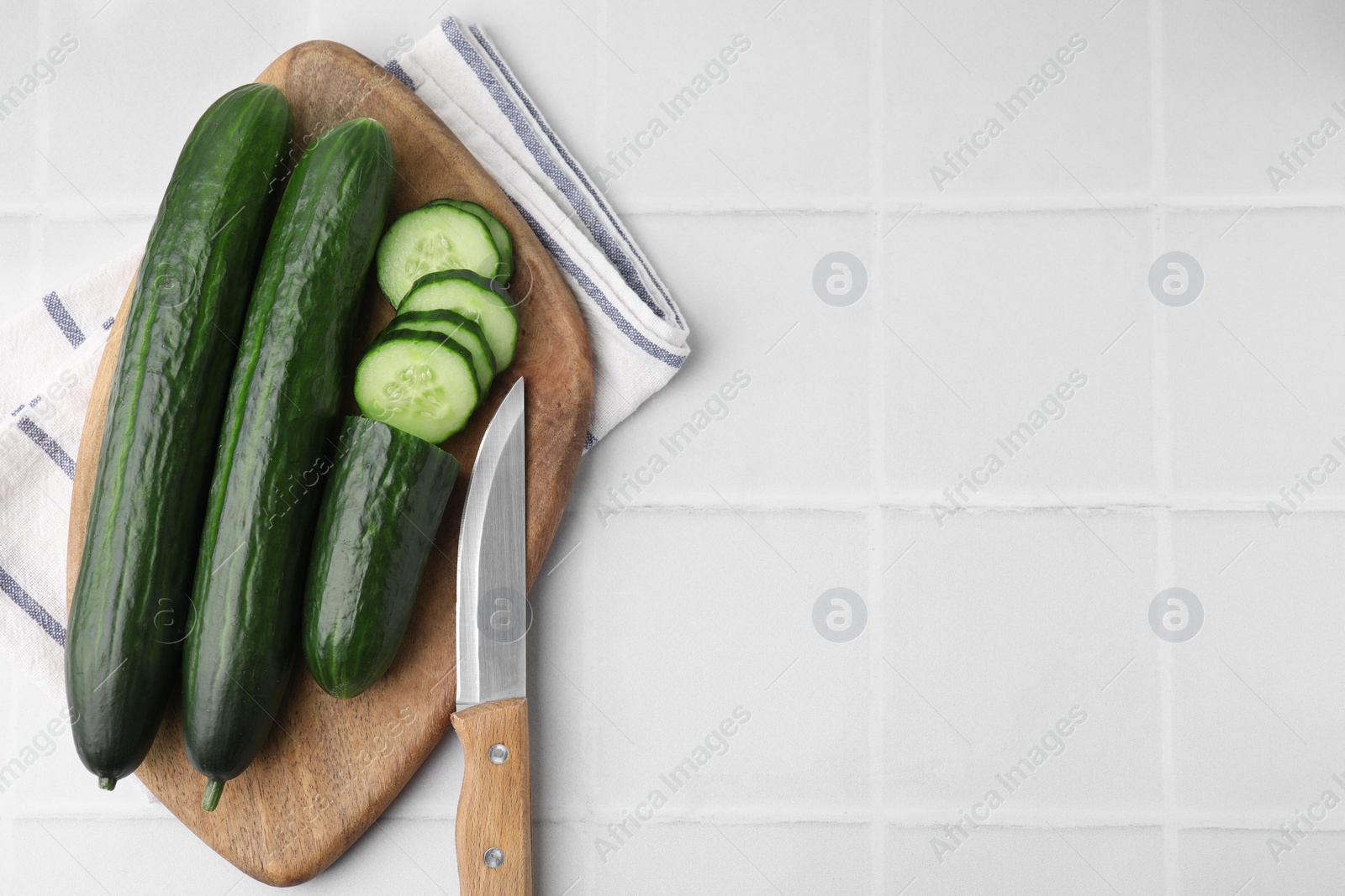 Photo of Fresh cucumbers and knife on white tiled table, top view. Space for text