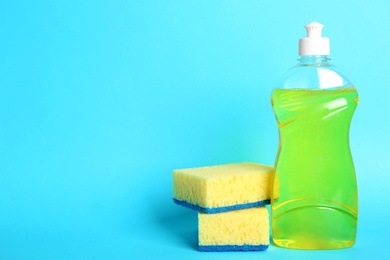 Detergent and sponges on light blue background, space for text