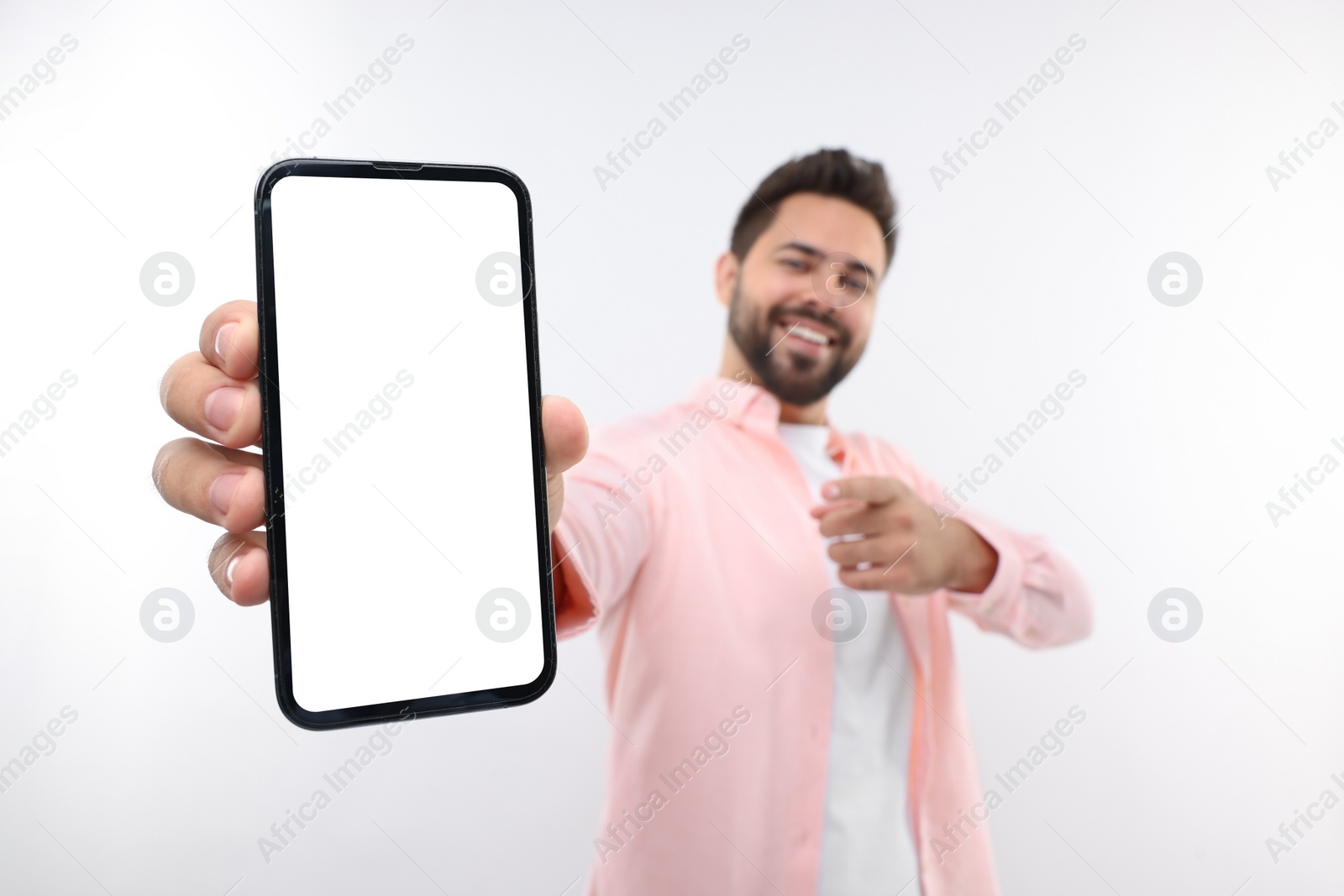 Photo of Young man showing smartphone in hand and pointing at it on white background, selective focus. Mockup for design