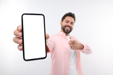 Photo of Young man showing smartphone in hand and pointing at it on white background, selective focus. Mockup for design