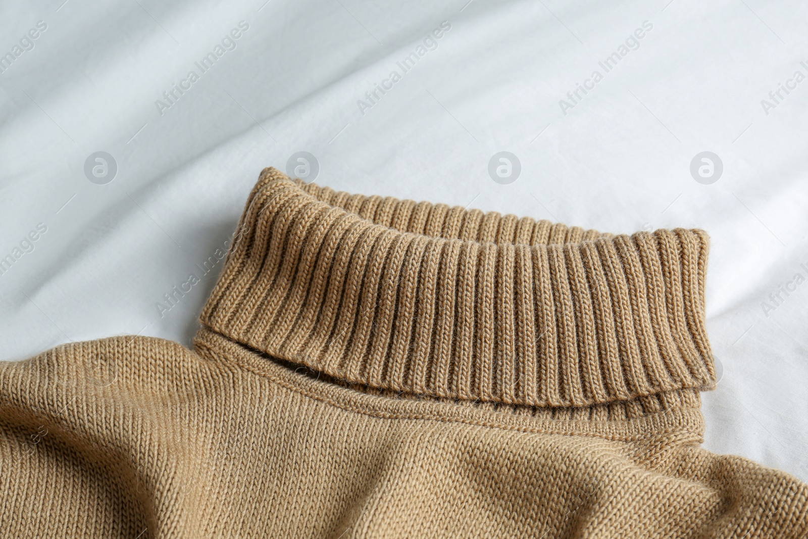 Photo of Stylish knitted sweater on white fabric, closeup