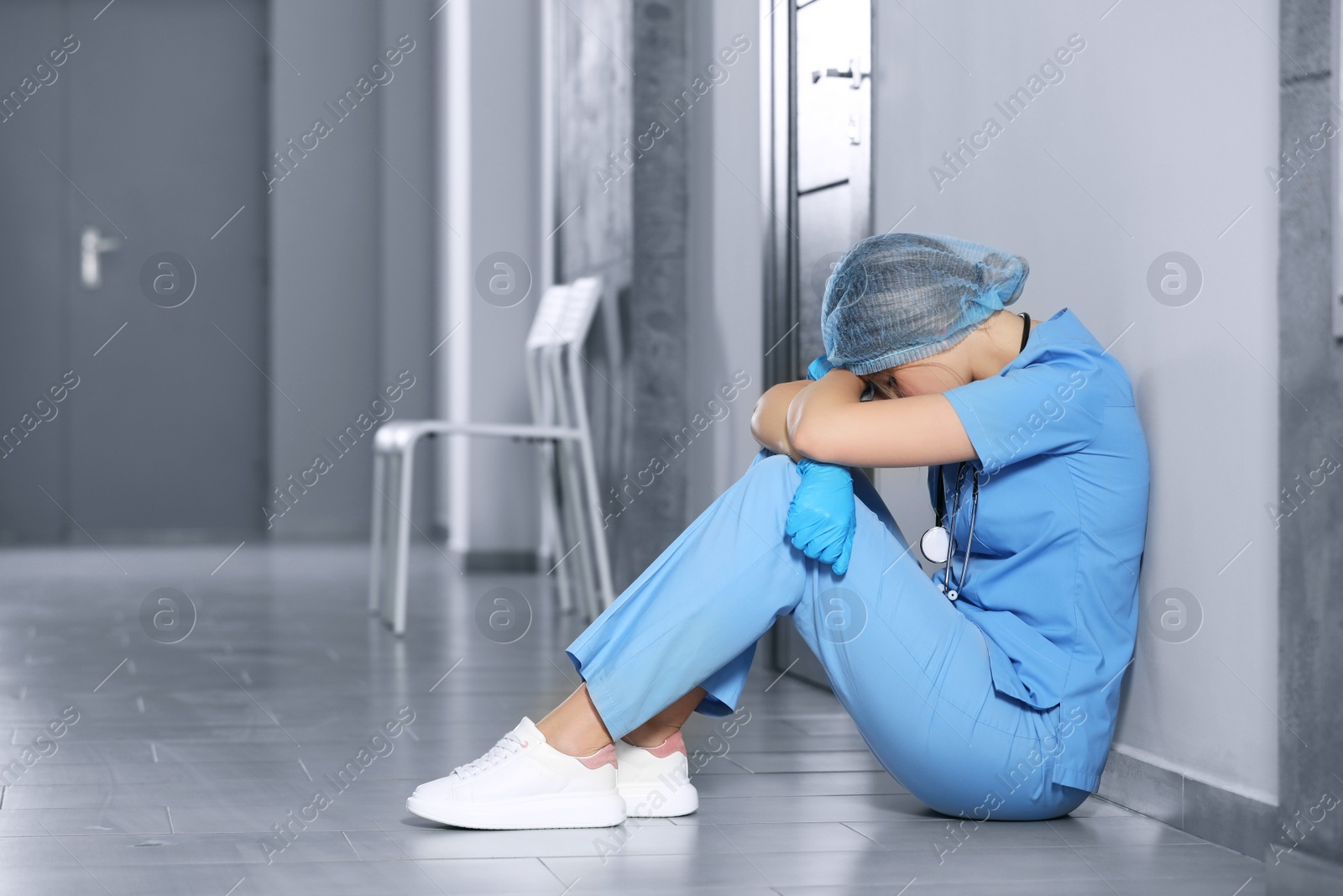 Photo of Exhausted doctor sitting on floor in hospital, space for text