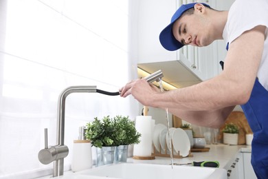 Photo of Young plumber examining metal faucet in kitchen