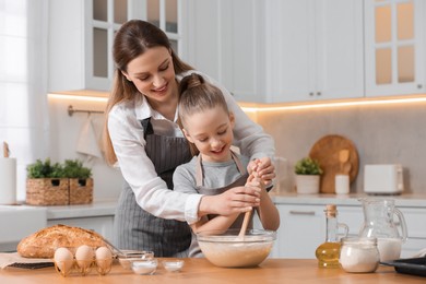 Making bread. Mother and her daughter preparing dough in bowl at wooden table in kitchen