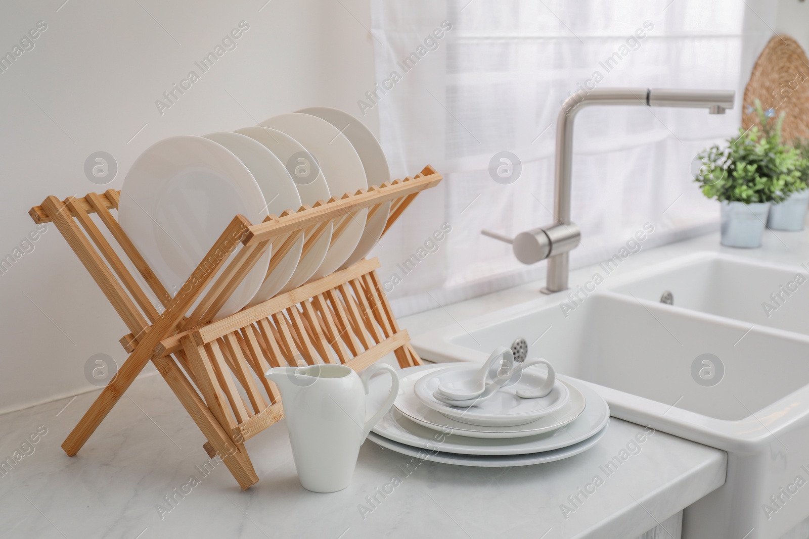 Photo of Drying rack with clean dishes on light marble countertop near sink in kitchen