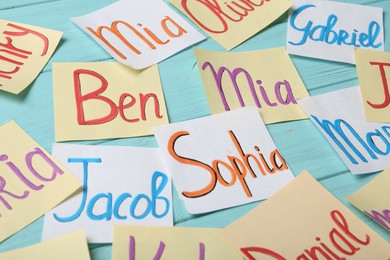 Photo of Paper notes with different baby names on light blue wooden table