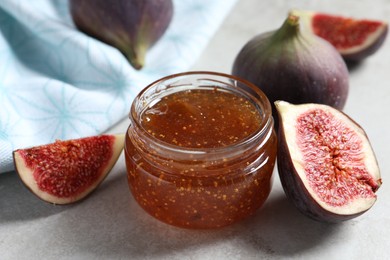 Jar of tasty sweet jam and fresh figs on light table, closeup