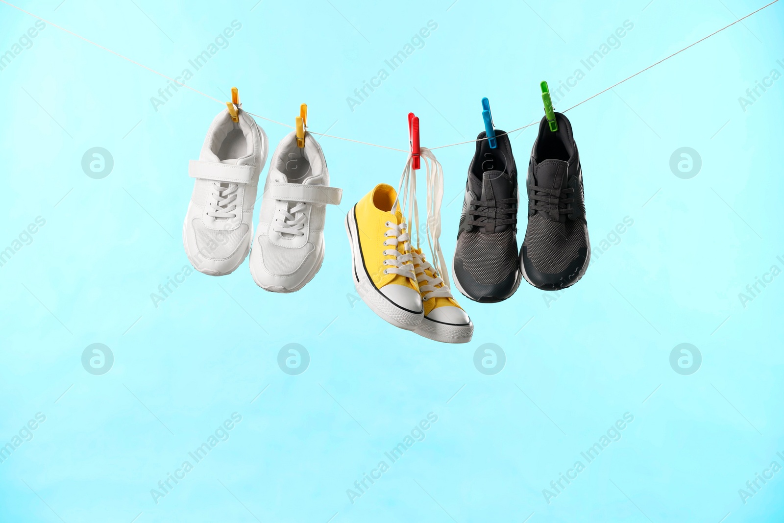 Photo of Different stylish sneakers drying on washing line against light blue background