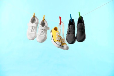 Photo of Different stylish sneakers drying on washing line against light blue background