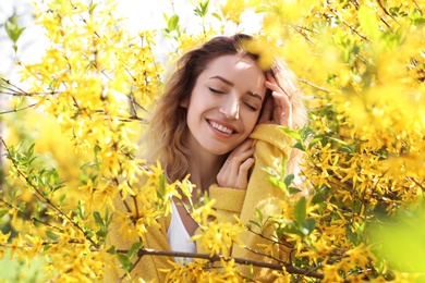 Attractive young woman posing near blossoming bush on sunny spring day