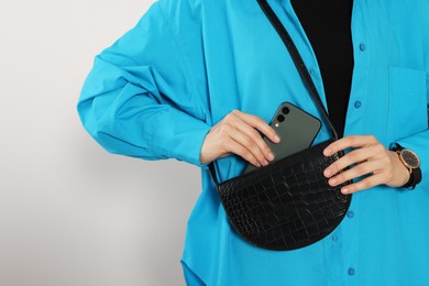 Photo of Woman putting smartphone into stylish bag on white background, closeup. Space for text
