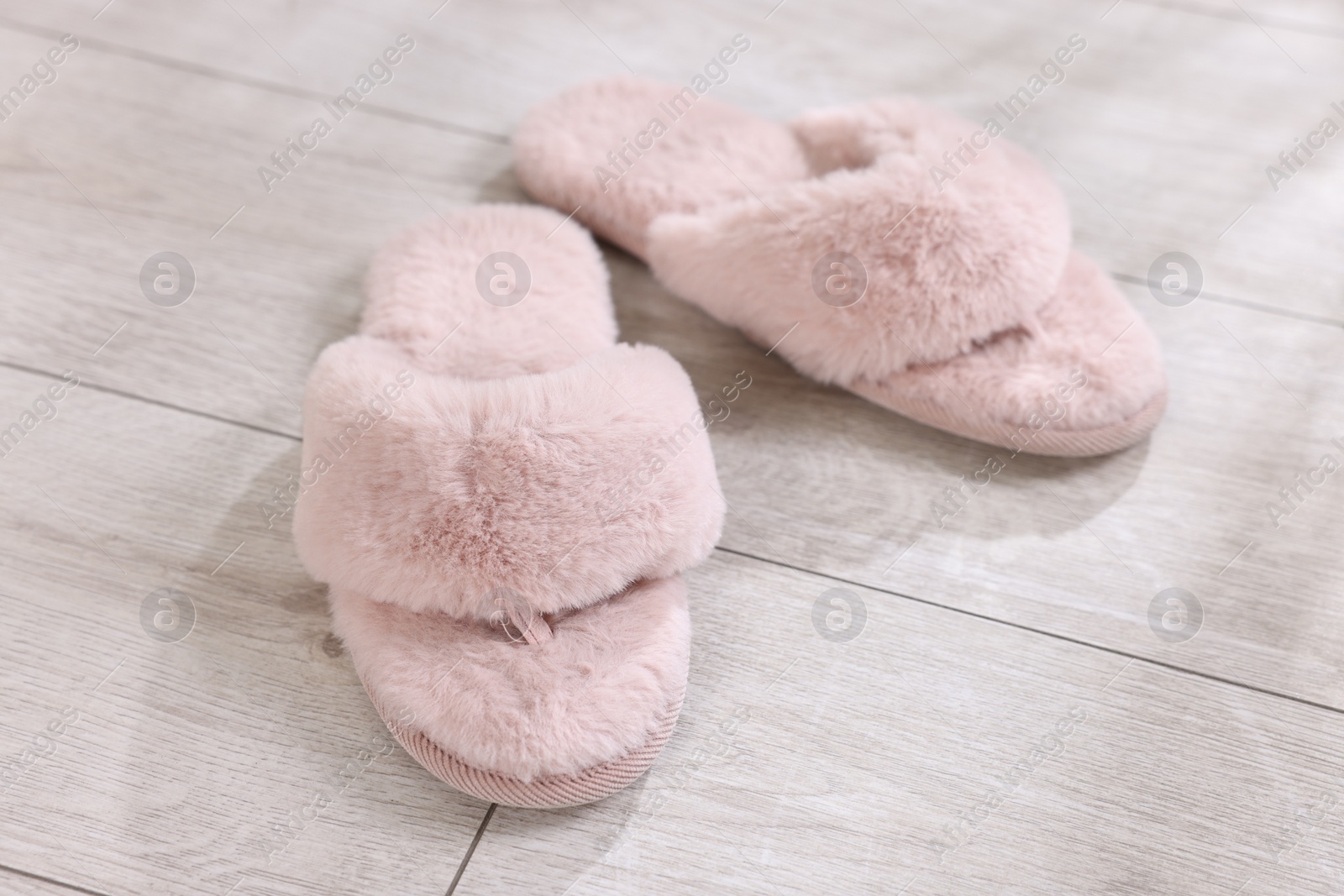 Photo of Pink soft slippers on light wooden floor at home, closeup