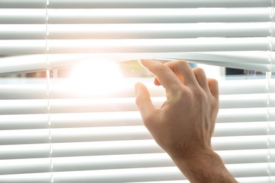 Photo of Young man opening window blinds, closeup. Space for text