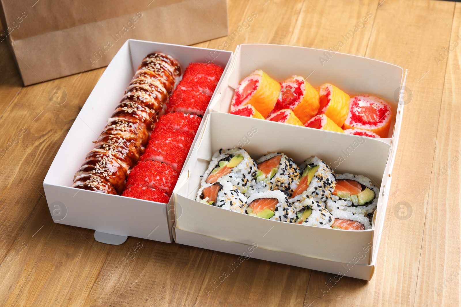 Photo of Food delivery. Paper boxes with delicious sushi rolls on wooden table