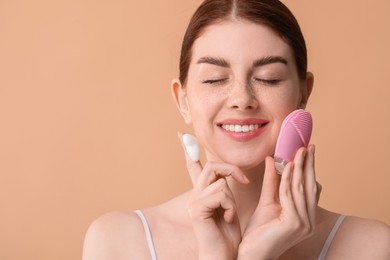 Photo of Washing face. Young woman with brush and cleansing foam on beige background, space for text