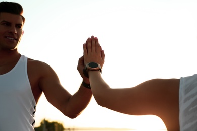Photo of Couple with fitness trackers giving each other high fives after training outdoors, closeup