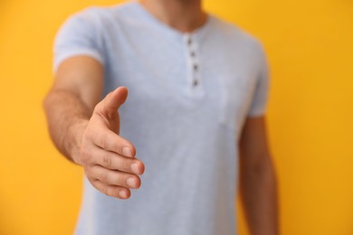 Man reaching out for handshake on yellow background, closeup