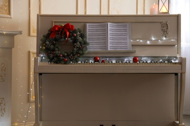 White piano with beautiful Christmas wreath and music sheets indoors
